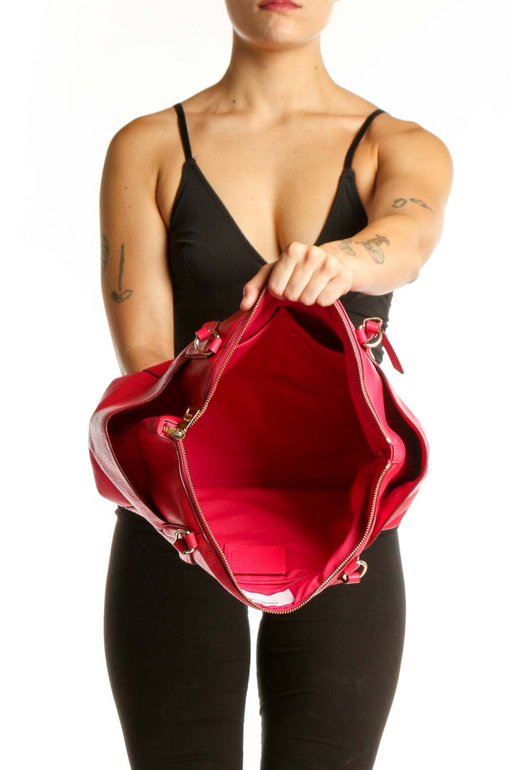 Back view of pink Coach leather shoulder tote bag worn on woman's shoulder, showing structured silhouette and side pockets