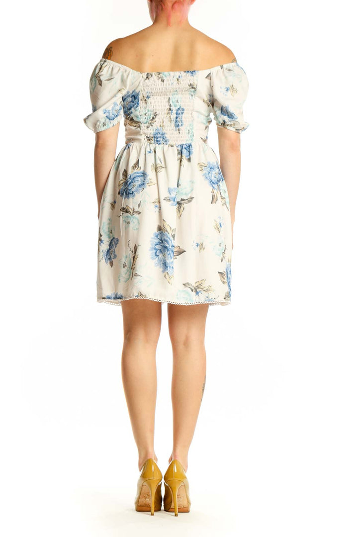 Back view of cream floral off-shoulder dress showing gathered neckline and knee-length hemline with decorative trim