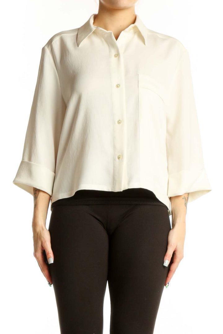 Woman wearing cream button-up collared blouse with three-quarter sleeves and chest pocket, paired with black pants