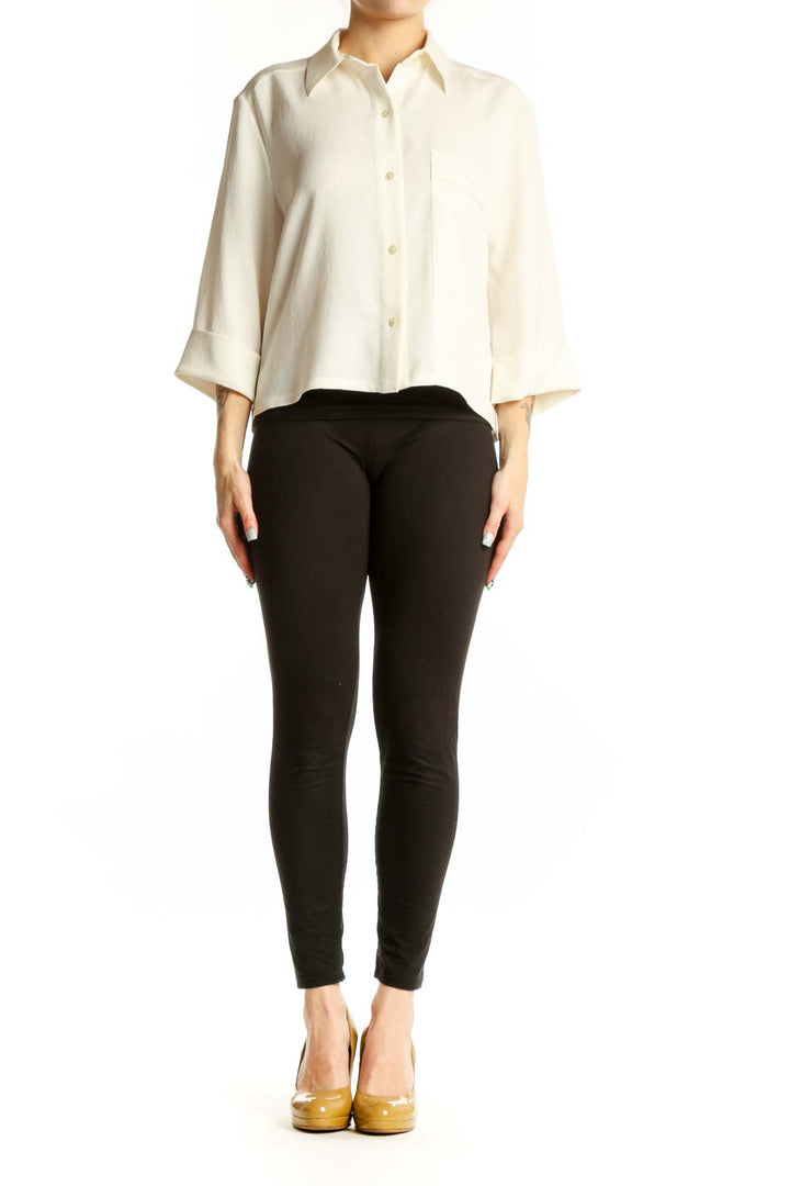 Woman wearing cream button-up collared blouse with three-quarter sleeves and chest pocket, paired with black pants