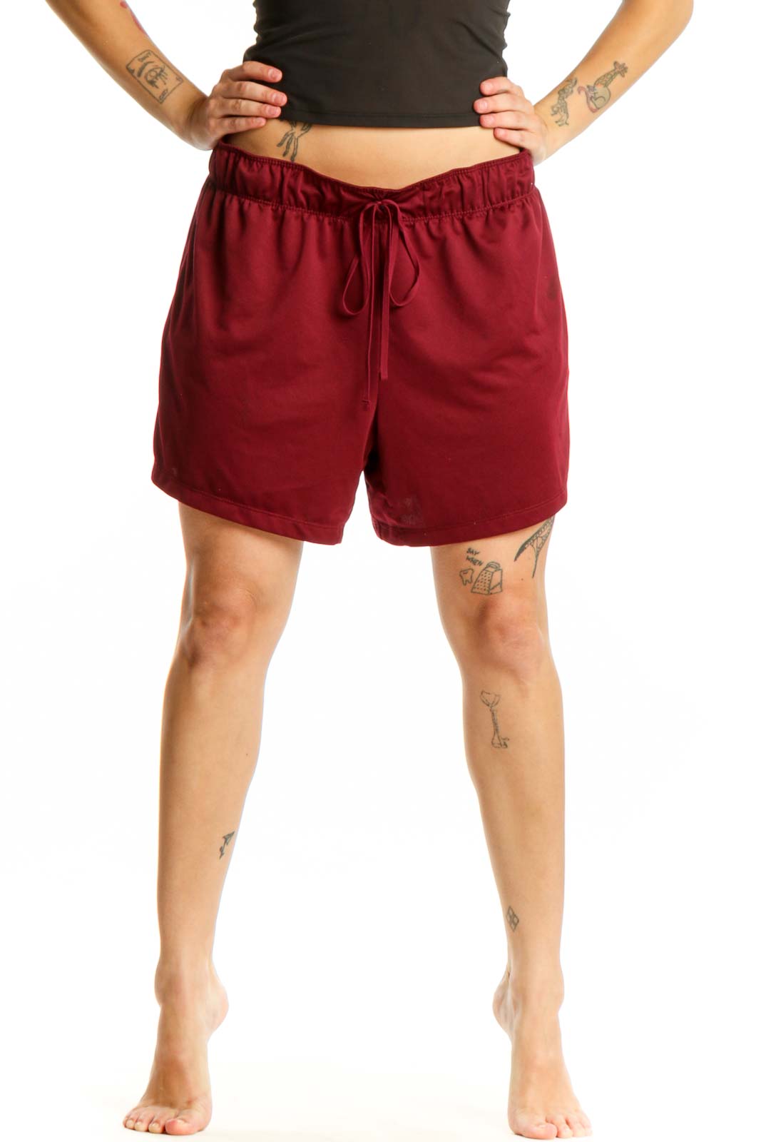 Front view of burgundy Nike athletic shorts with elastic waistband and drawstring closure, paired with black crop top
