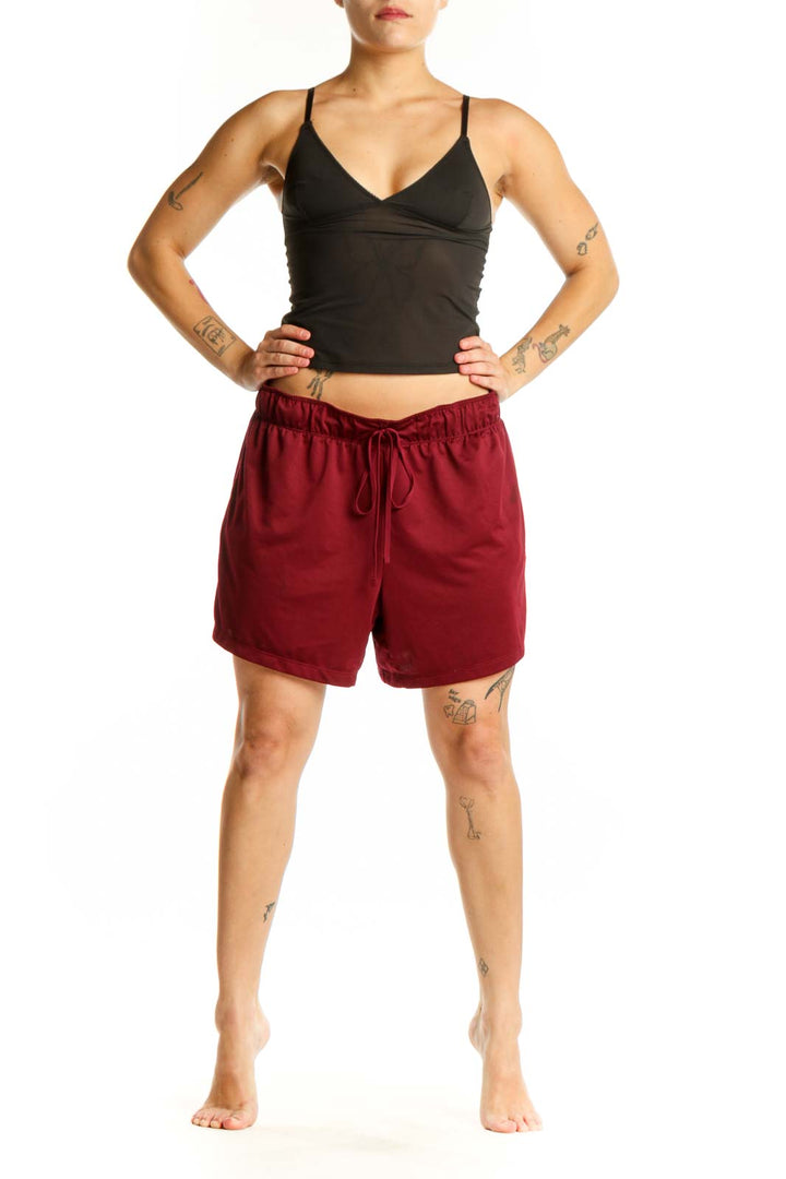 Front view of burgundy Nike athletic shorts with elastic waistband and drawstring closure, paired with black crop top