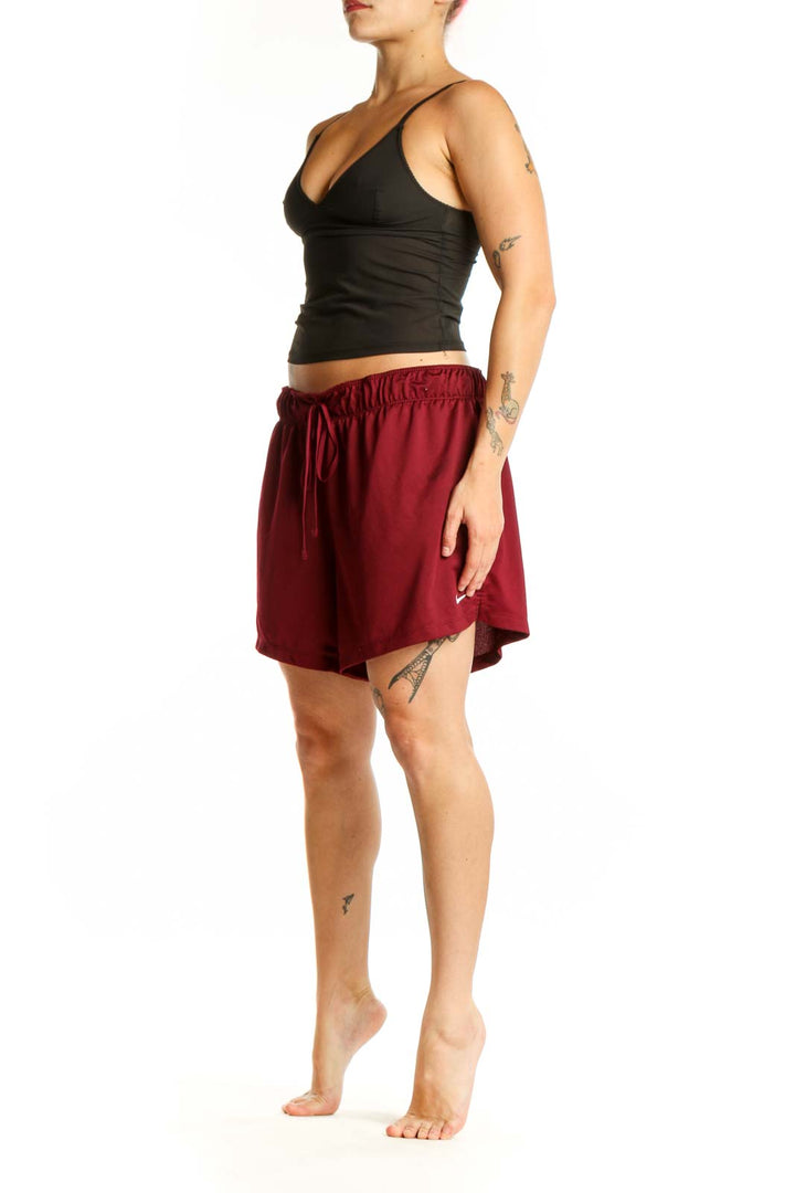 Front view of burgundy Nike athletic shorts with elastic waistband and drawstring closure, paired with black crop top