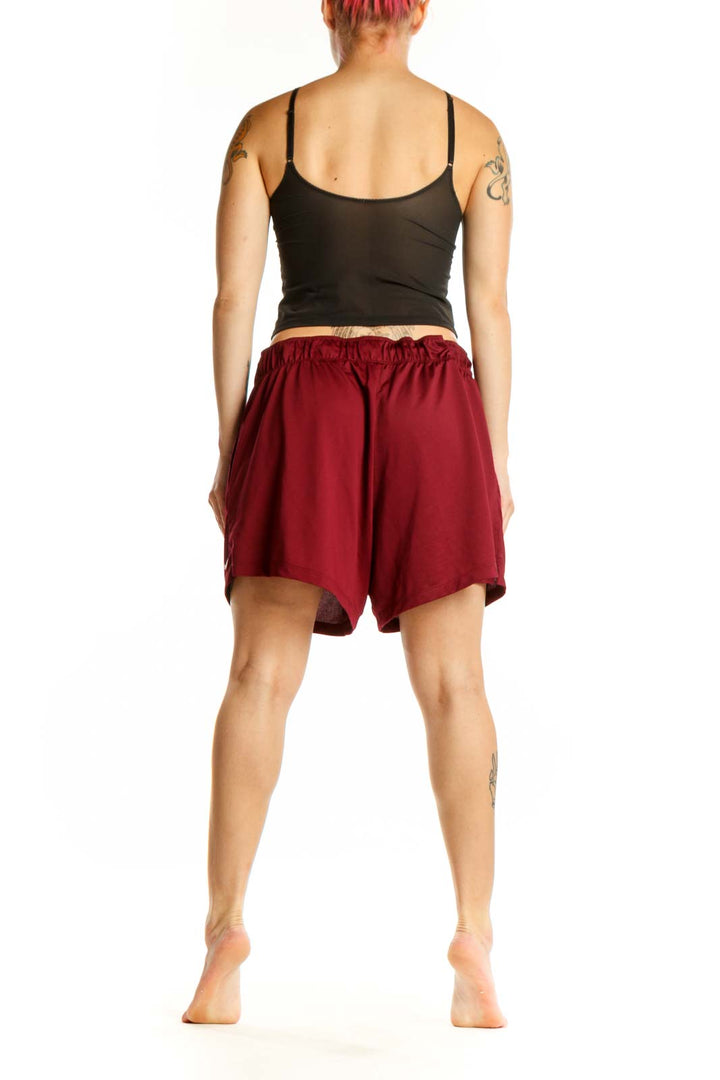 Back view of burgundy Nike athletic shorts showing relaxed fit and length, styled with black sports bra