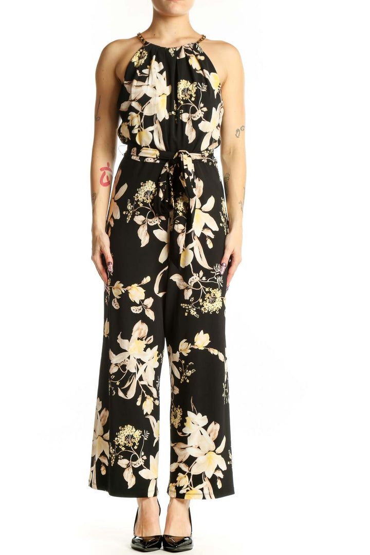 Black floral halter jumpsuit with cream and gold botanical print, adjustable tie waist, and wide-leg silhouette, front view