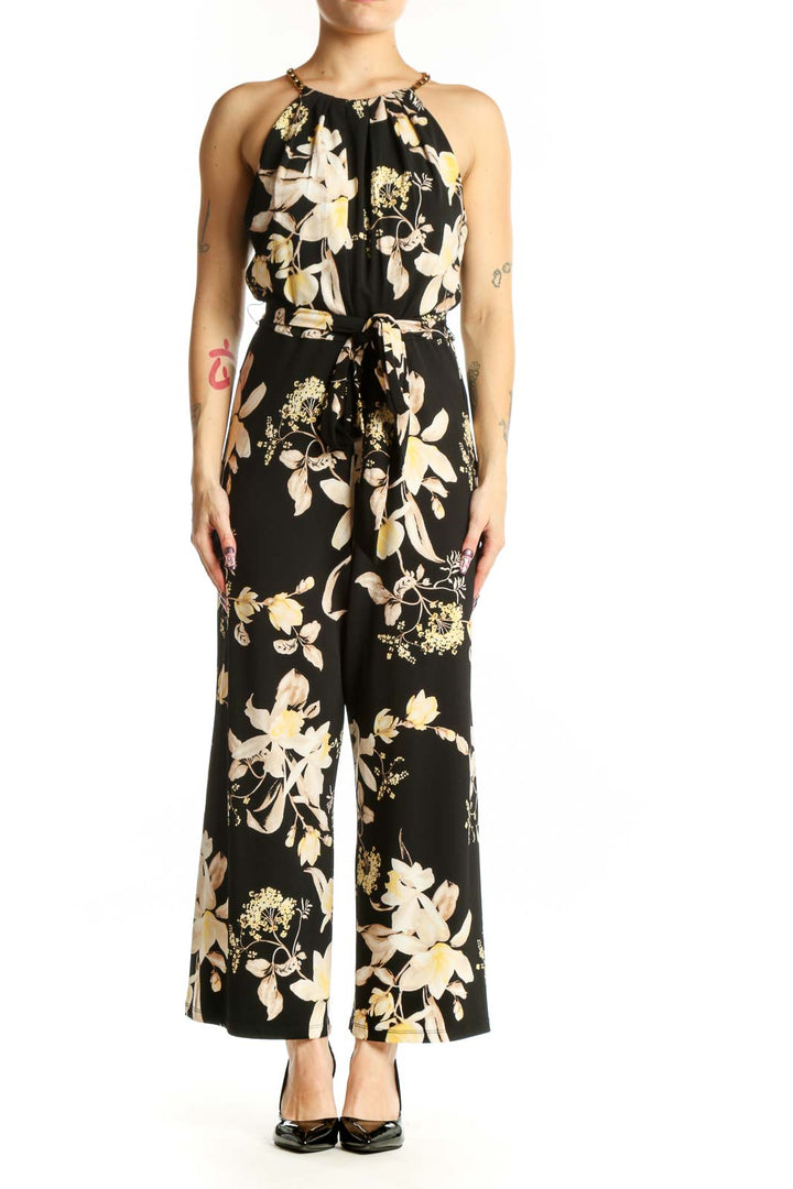 Black floral halter jumpsuit with cream and gold botanical print, adjustable tie waist, and wide-leg silhouette, front view