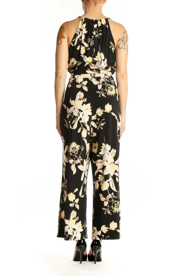 Black floral halter jumpsuit with cream and gold botanical print, adjustable tie waist, and wide-leg silhouette, back view