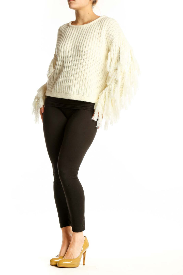 Cream ribbed knit sweater with fringe-detailed sleeves, cropped length, worn with black pants