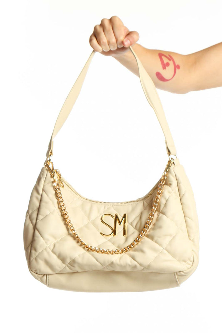Cream quilted shoulder bag by Steve Madden with gold chain detail and SM logo charm, held by model