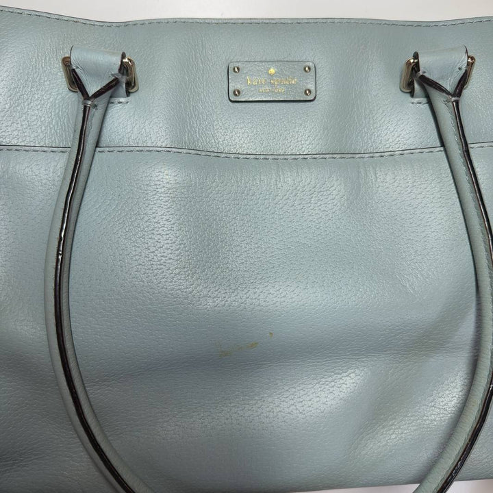Tag view of mint green Kate Spade tote bag worn by model, showing structured design and handles