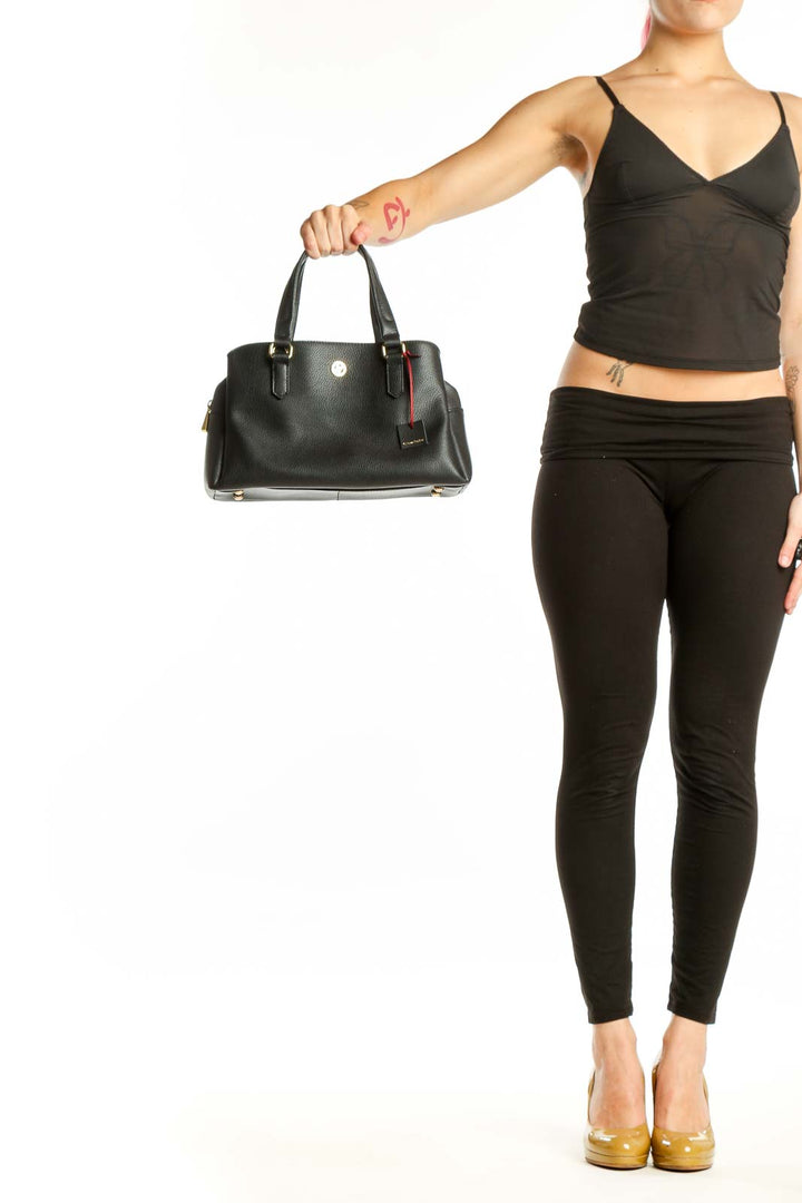 Black leather satchel bag with dual handles and red trim detail held by hand, showing front view with gold-tone hardware