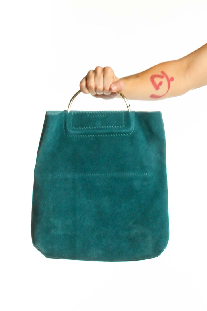 Teal suede clutch with top handle held in hand, showing front view and embossed flap detail