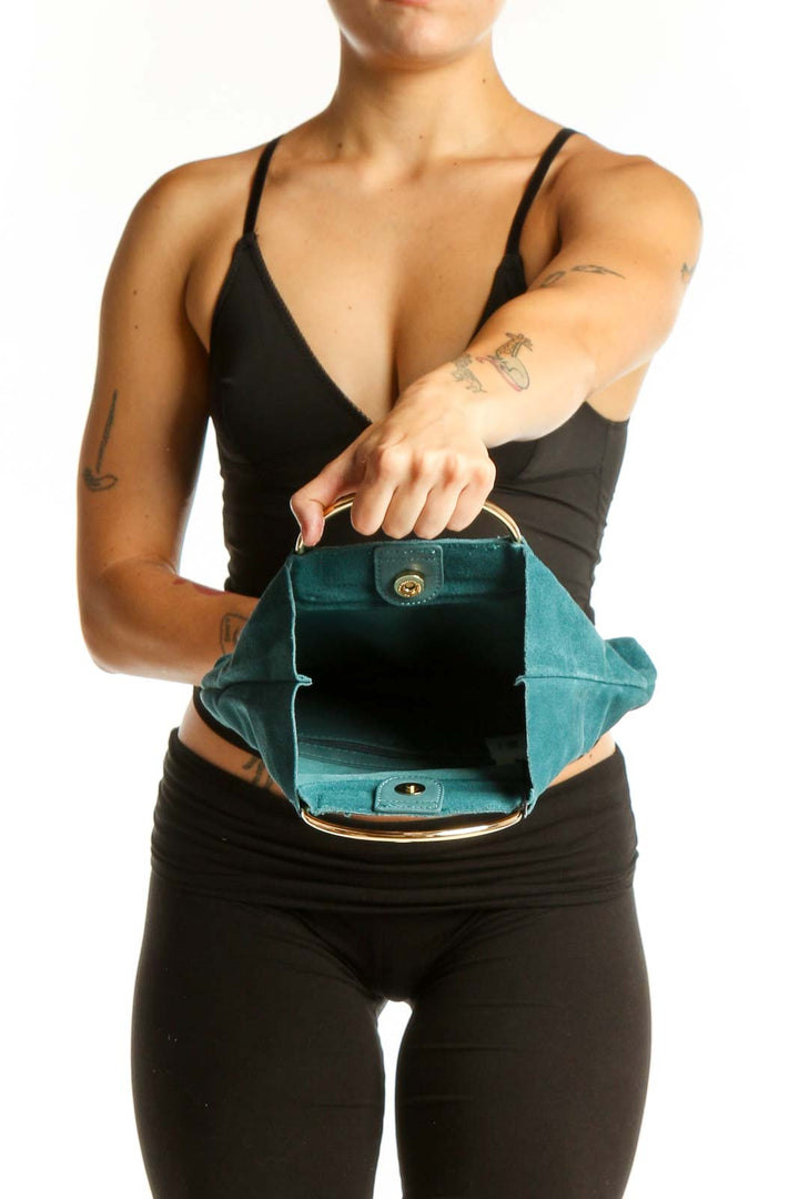 Teal suede clutch with top handle displayed from side angle, worn with black outfit