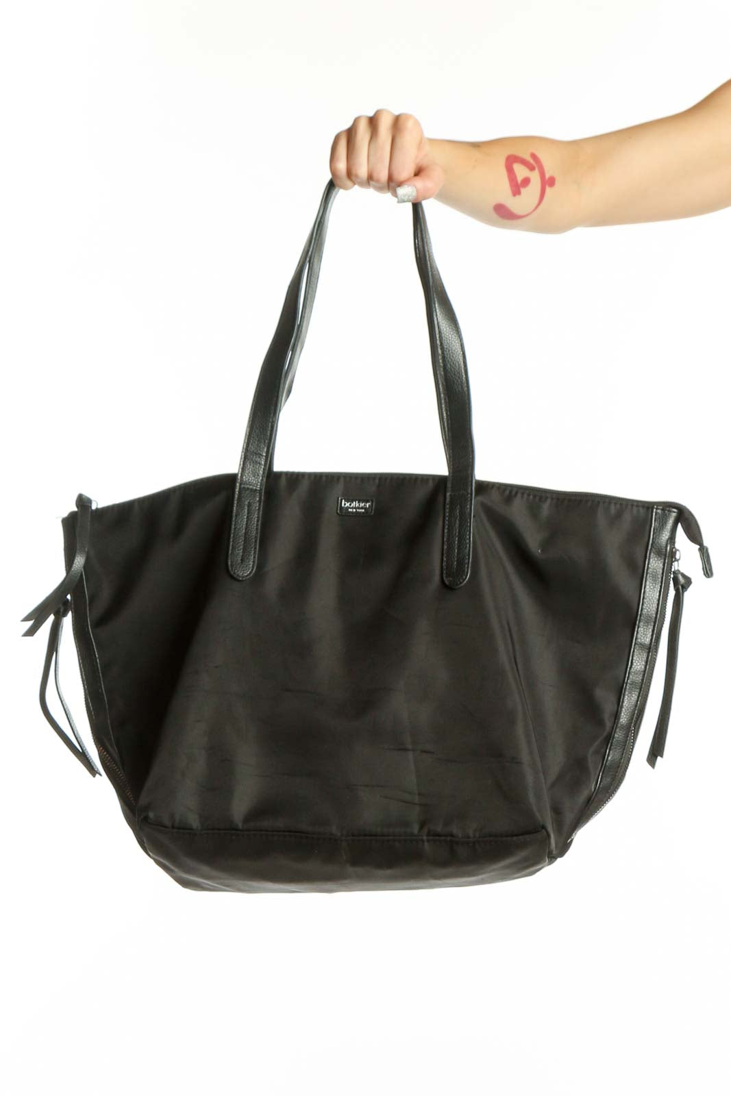 Black Botkier nylon tote bag with dual handles held by hand, showing front view with adjustable side ties
