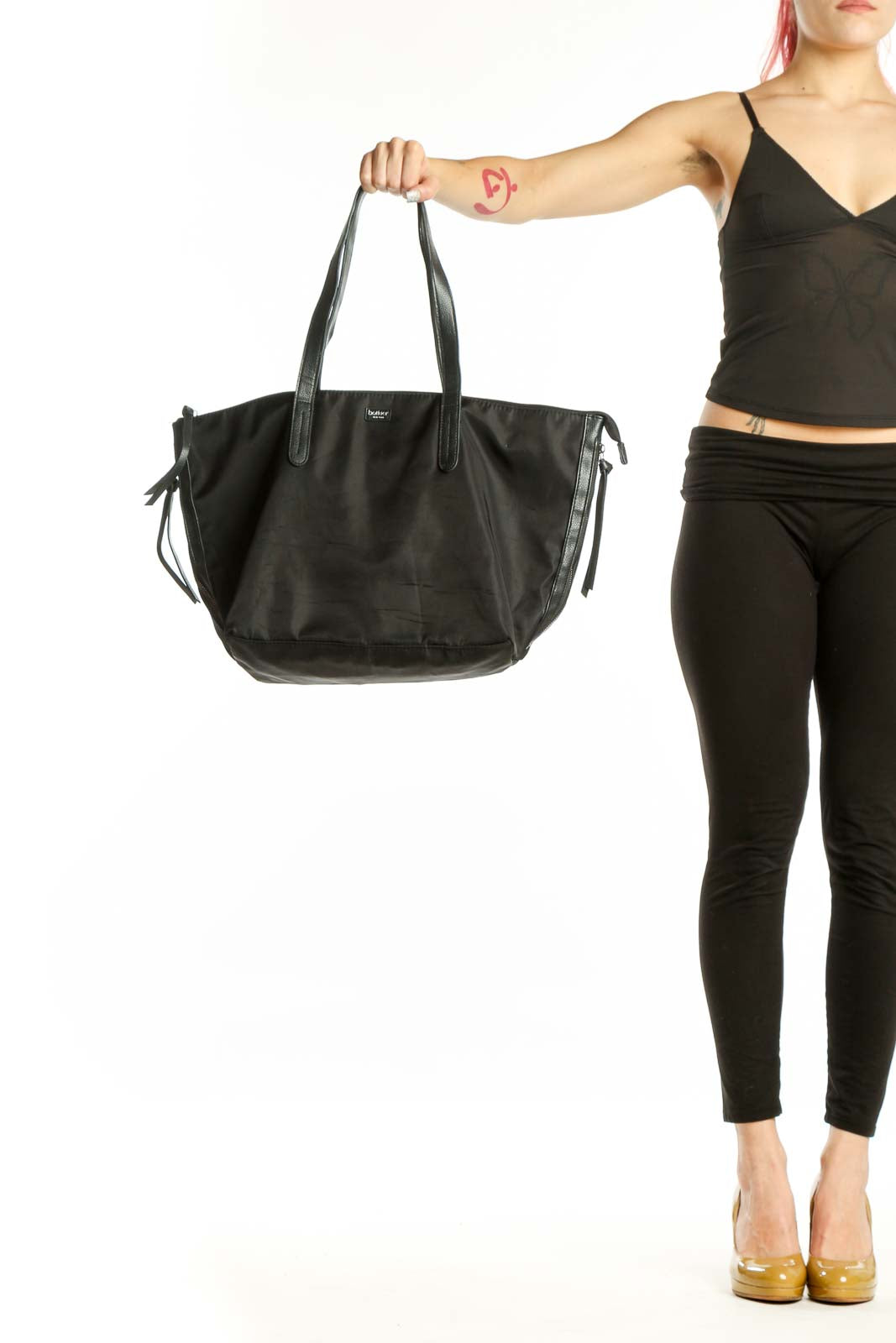 Black Botkier nylon tote bag with dual handles held by hand, showing front view with adjustable side ties