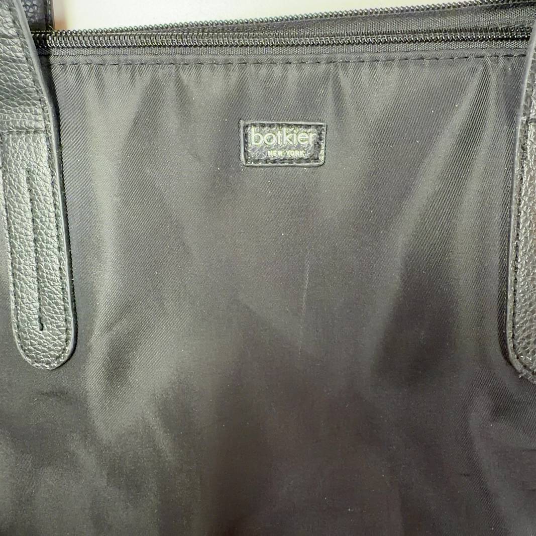 Tag view of black Botkier tote bag worn on shoulder, displaying spacious interior and structured silhouette