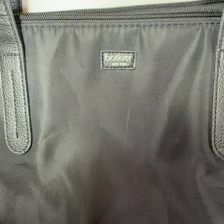 Tag view of black Botkier tote bag worn on shoulder, displaying spacious interior and structured silhouette