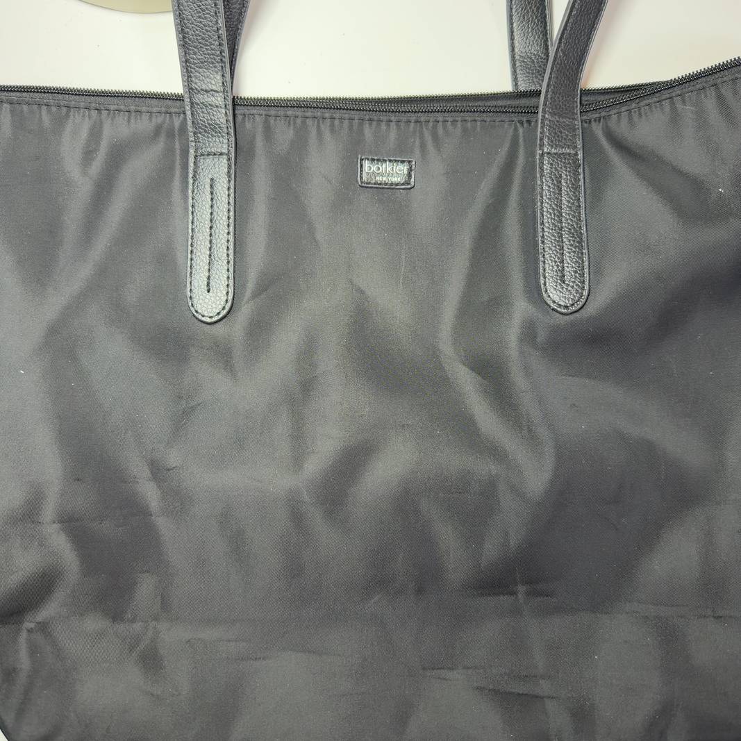 Tag view of black Botkier tote bag worn on shoulder, displaying spacious interior and structured silhouette