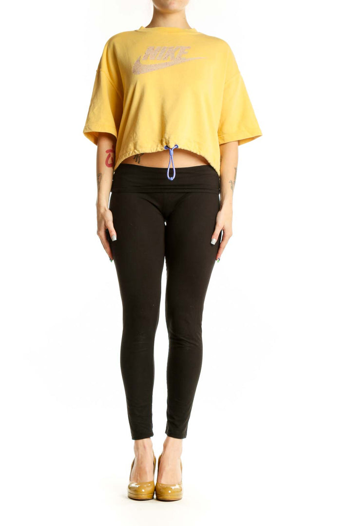 Yellow Nike cropped athletic t-shirt with metallic swoosh logo worn with black leggings, front view
