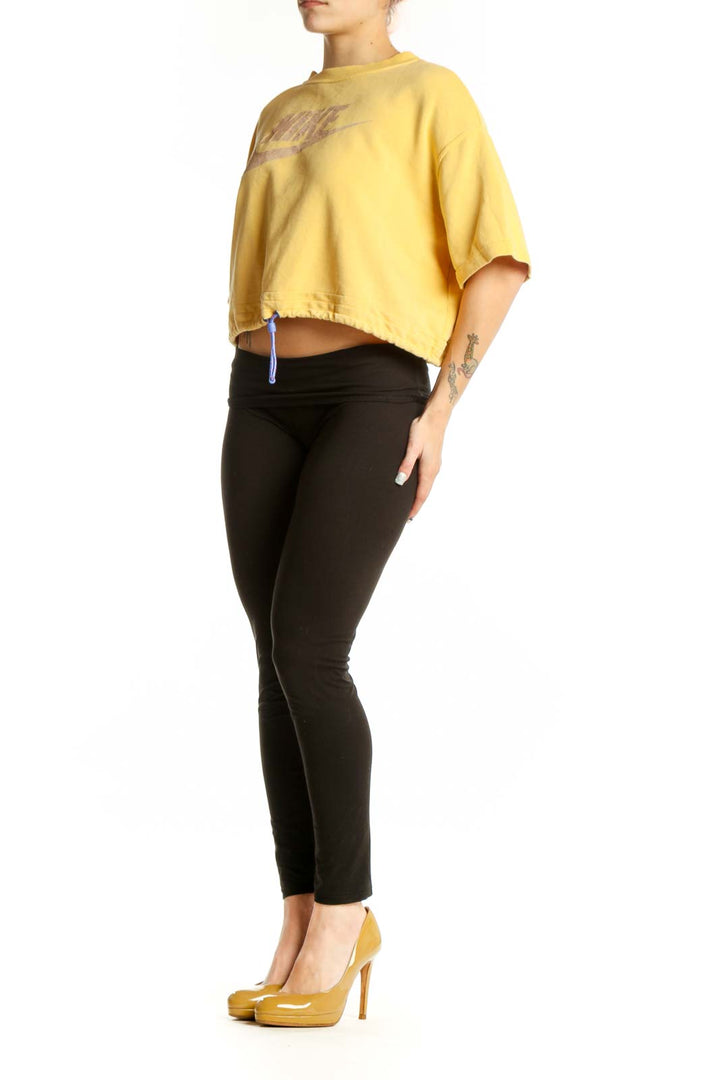 Yellow Nike cropped athletic t-shirt with metallic swoosh logo worn with black leggings, front view