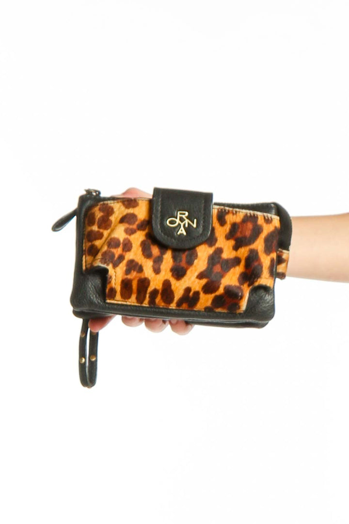 ORYAN orange and black leopard print clutch with black leather trim and wristlet strap, held in hand