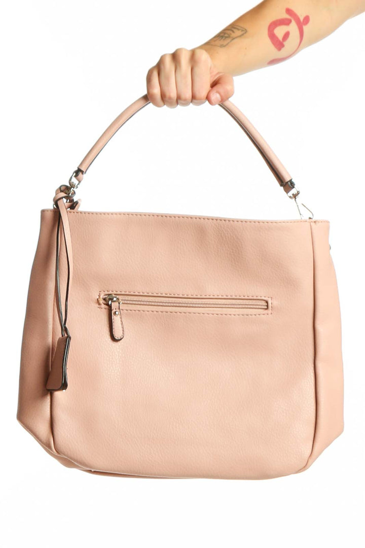 Blush pink leather crossbody bag with front zip pocket and adjustable shoulder strap, held by hand
