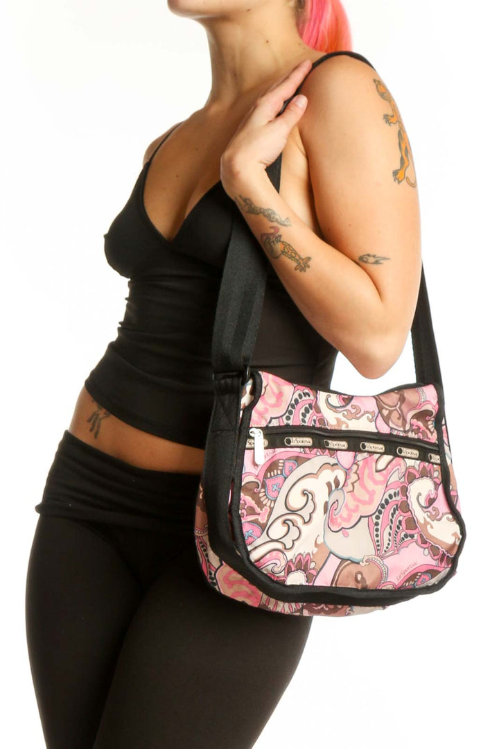 Pink paisley Lesportsac crossbody bag with black adjustable strap and multiple organizational pockets, front view