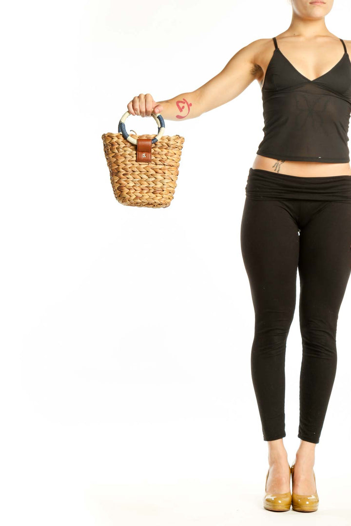 Tan woven straw crossbody basket bag with cognac leather accent and navy-wrapped handles held in hand