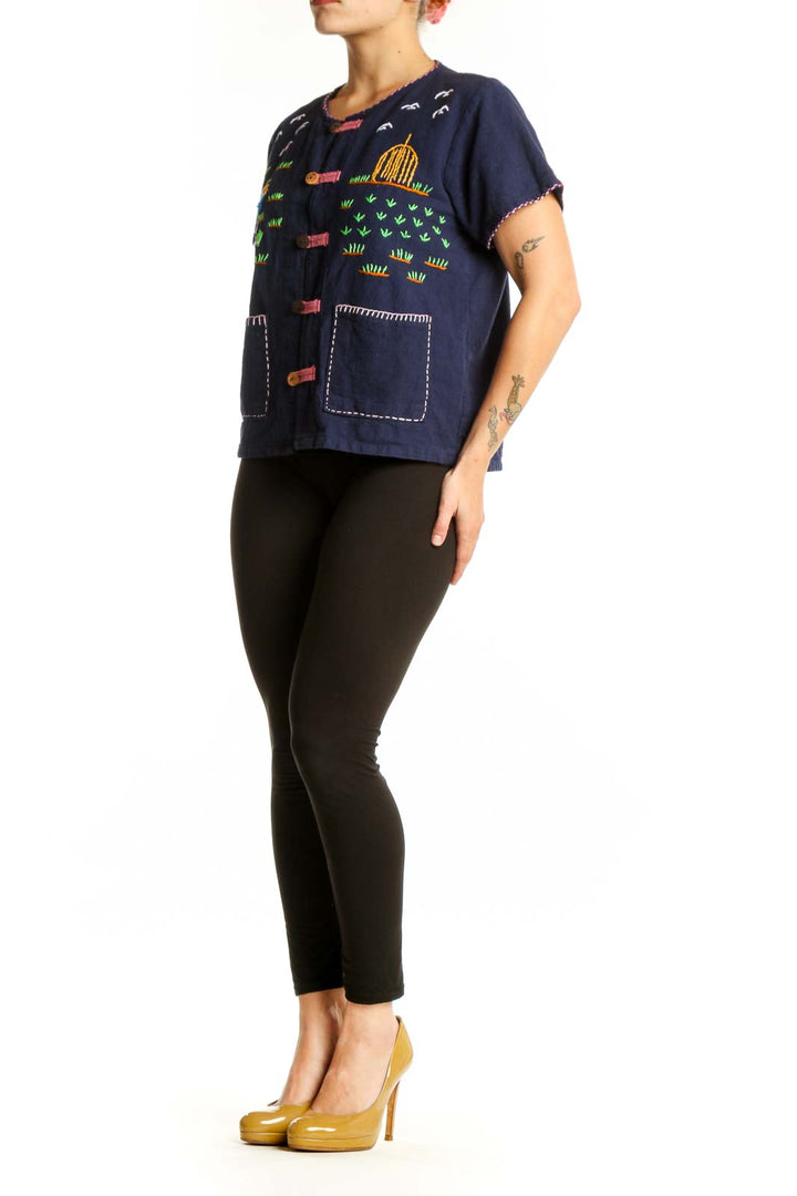 Navy SilkRoll embroidered button-up top with colorful hand-stitched designs including children, suns, and grass motifs, coral buttons, and white stitched patch pockets