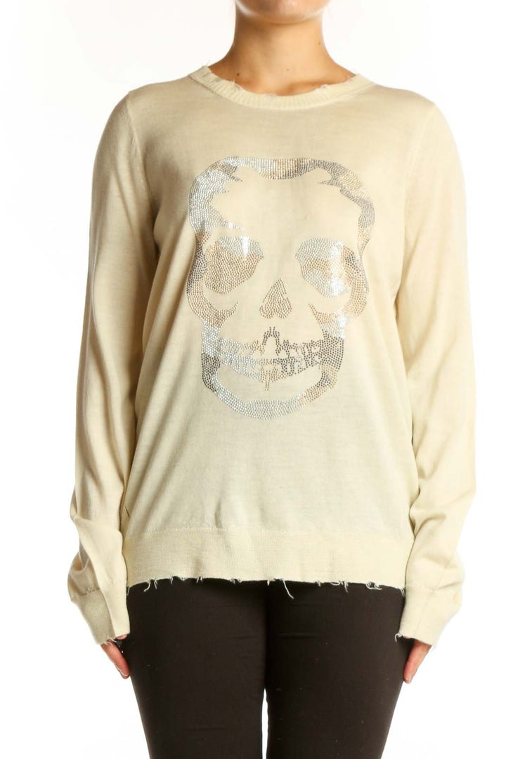 Cream merino wool sweater with shimmering silver skull graphic on front, distressed hem detail