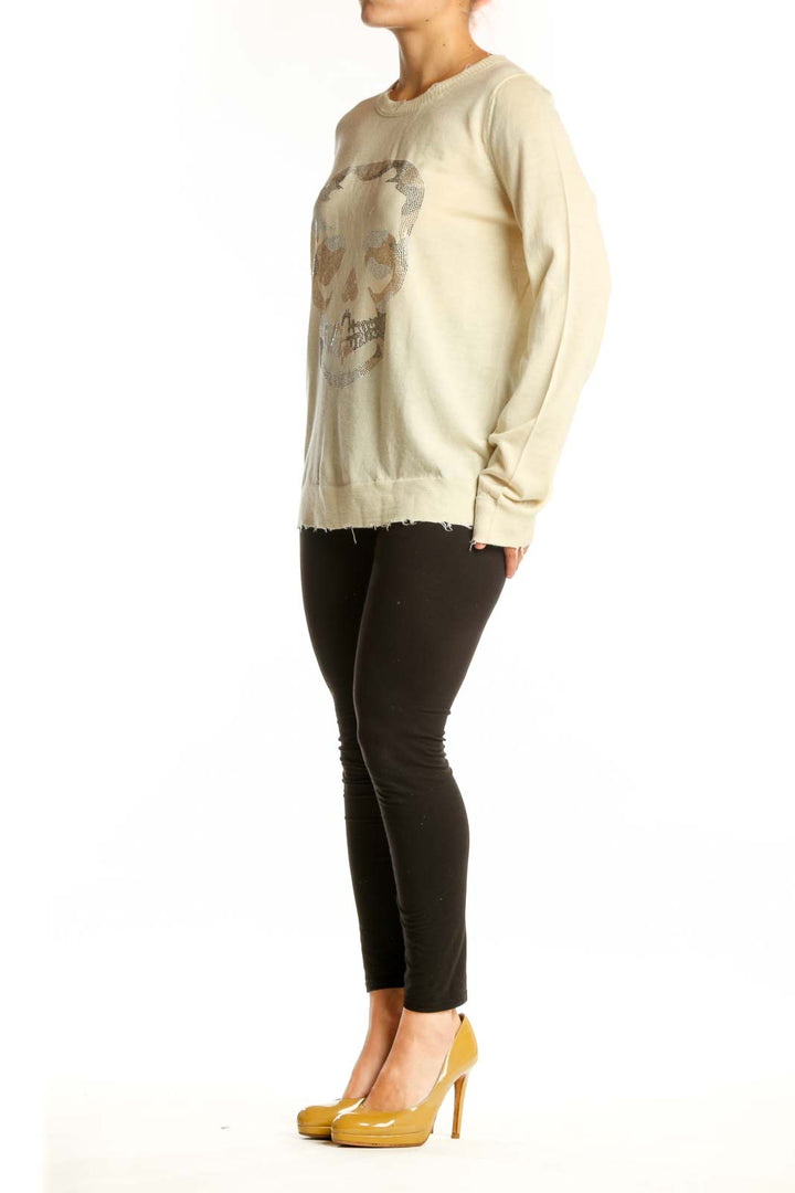 Cream merino wool sweater with shimmering silver skull graphic on front, distressed hem detail
