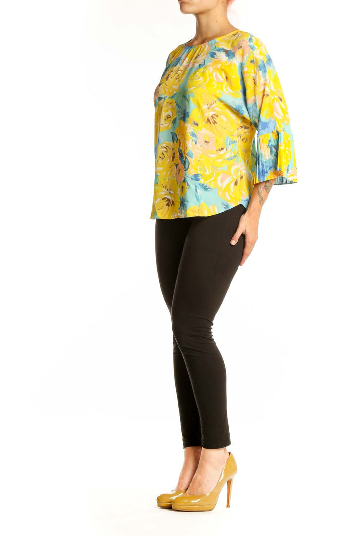 Yellow floral pleated bell sleeve top by Sioni with blue and coral flowers, worn with black pants