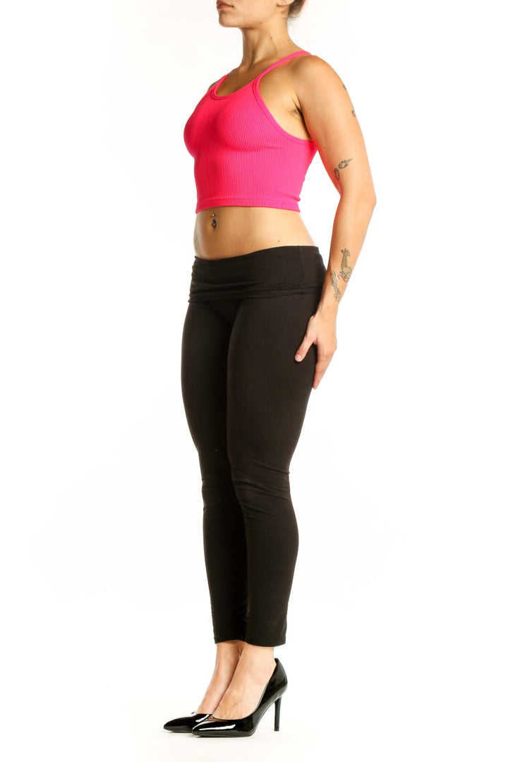 Woman wearing pink ribbed crop tank top with racerback design and black leggings, front view