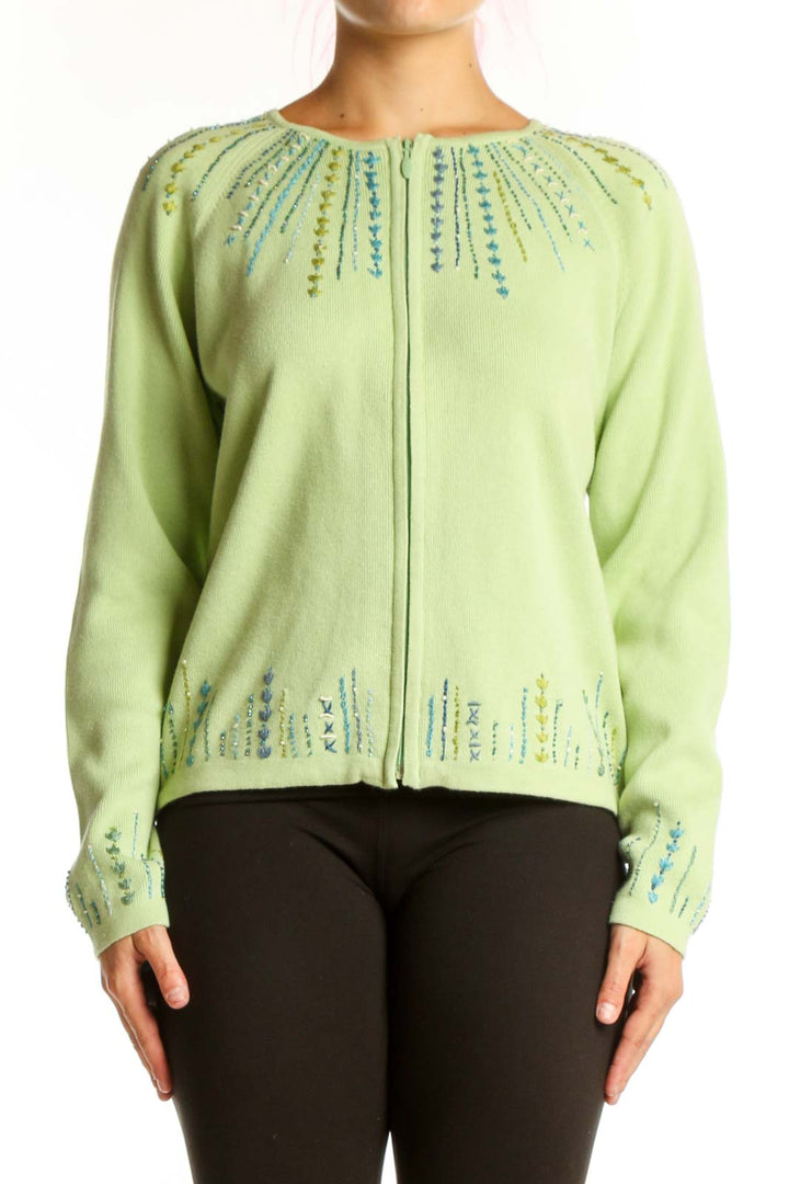 Lime green cotton cardigan with embroidered teal and blue details on neckline and cuffs, worn with black pants