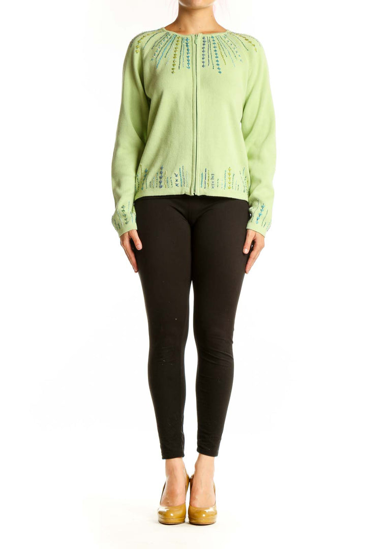 Lime green cotton cardigan with embroidered teal and blue details on neckline and cuffs, worn with black pants