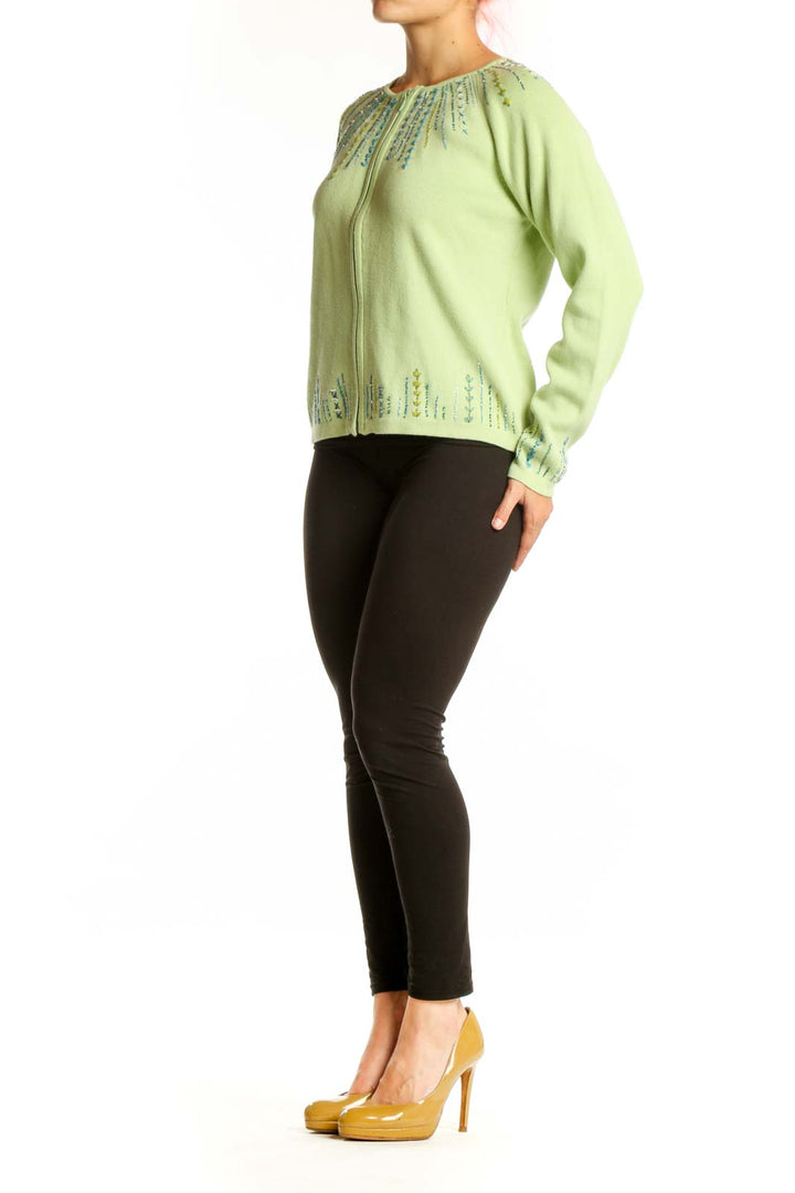 Lime green cotton cardigan with embroidered teal and blue details on neckline and cuffs, worn with black pants