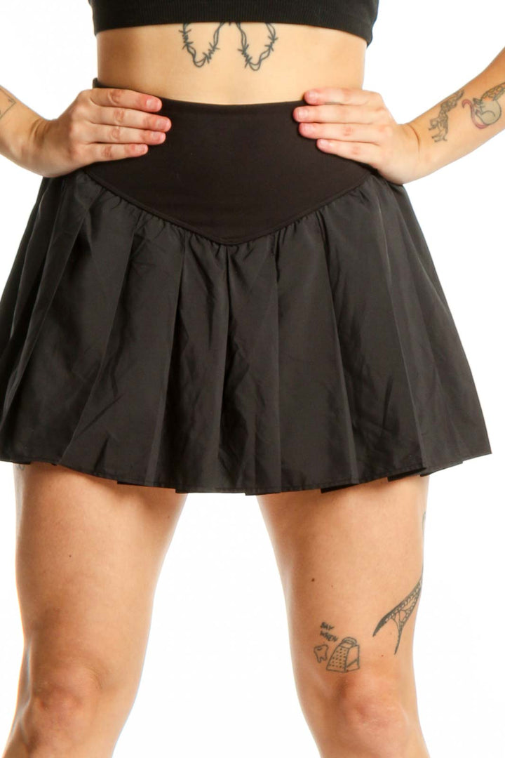 Black pleated athletic skirt with high waistband and built-in shorts, front view
