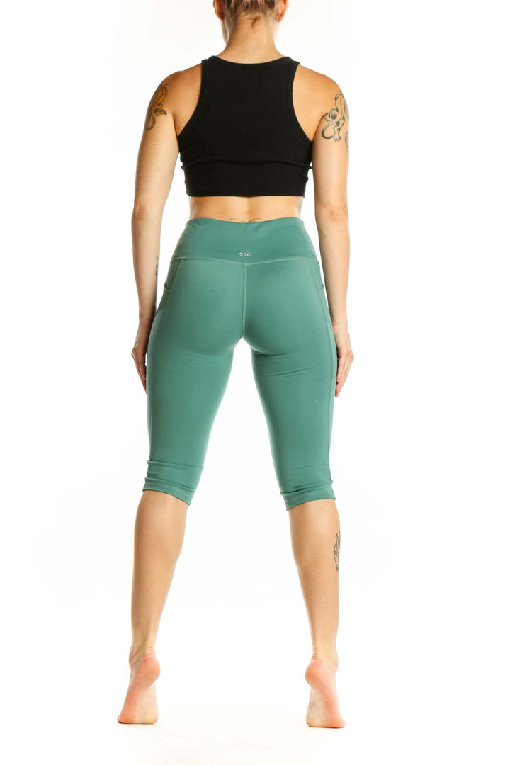 Woman wearing sage green high-waist capri leggings with black sports bra, side view showing fit