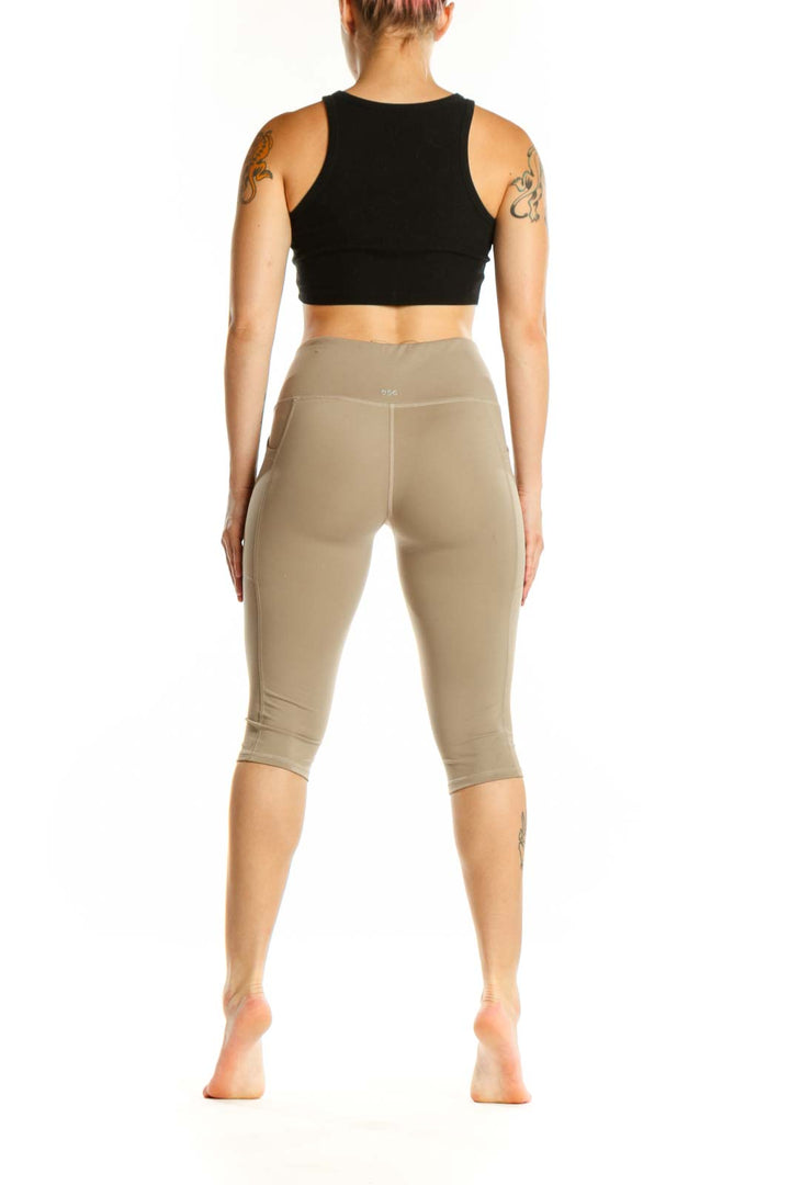 Woman wearing beige high-waist capri leggings with side pockets, back view showing fitted silhouette