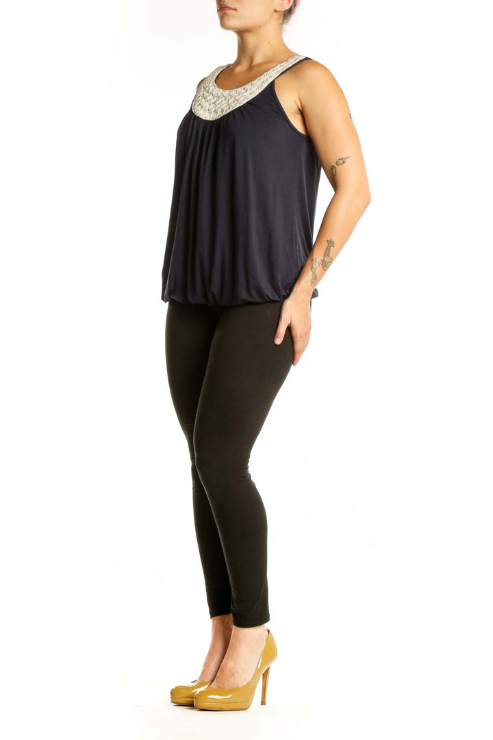 Navy sleeveless tank top with cream embellished beaded neckline and gathered front, worn with black pants