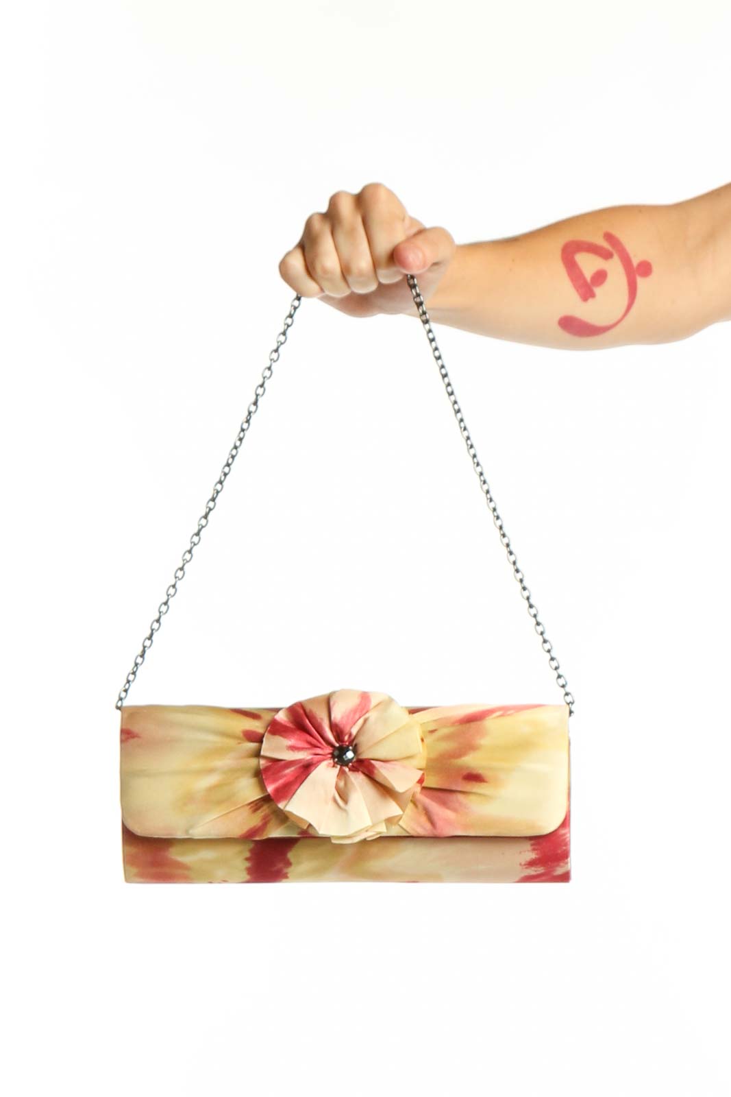 Cream silk shoulder bag with red and pink floral pattern and dimensional flower embellishment, held by hand with silver chain strap