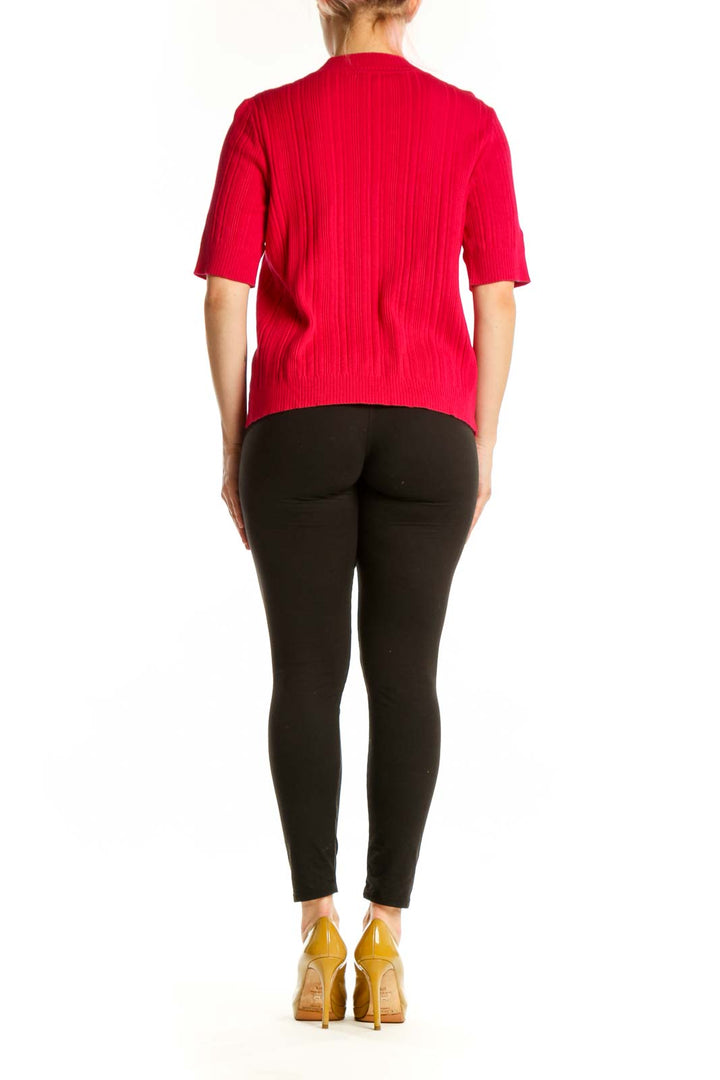Back view of red ribbed knit cardigan showing relaxed fit and drape, paired with black leggings and gold heels