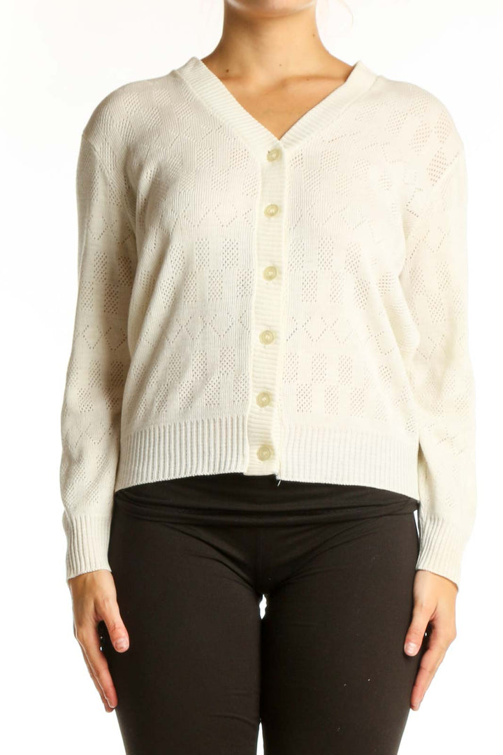 Cream cable knit cardigan with V-neckline and button-front closure, worn with black pants