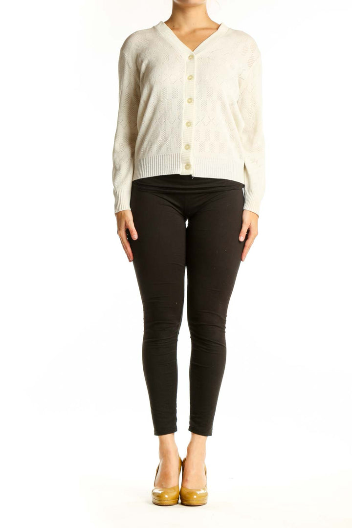 Cream cable knit cardigan with V-neckline and button-front closure, worn with black pants
