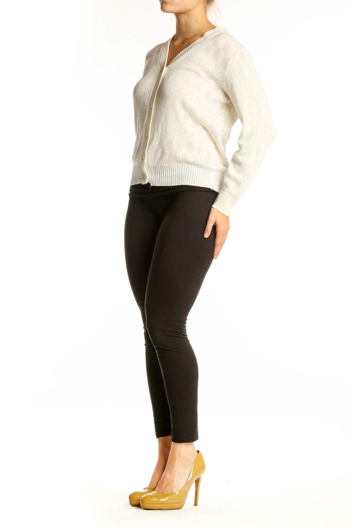 Cream cable knit cardigan with V-neckline and button-front closure, worn with black pants