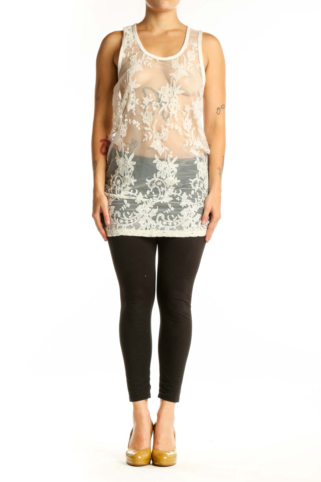 Cream lace tank top with intricate white floral lace detailing and sheer front design, worn with black leggings