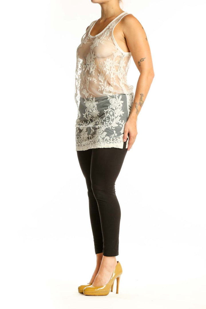 Cream lace tank top with intricate white floral lace detailing and sheer front design, worn with black leggings