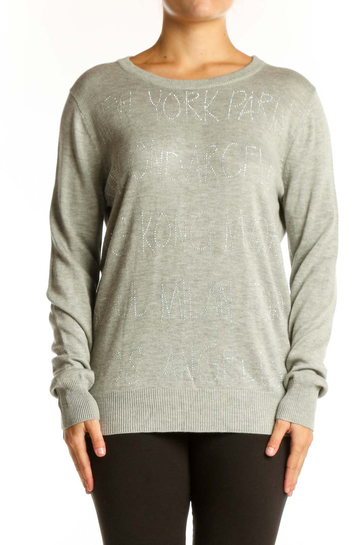 Beige cashmere blend knit pullover with embellished text detail, crew neckline, and long sleeves on model