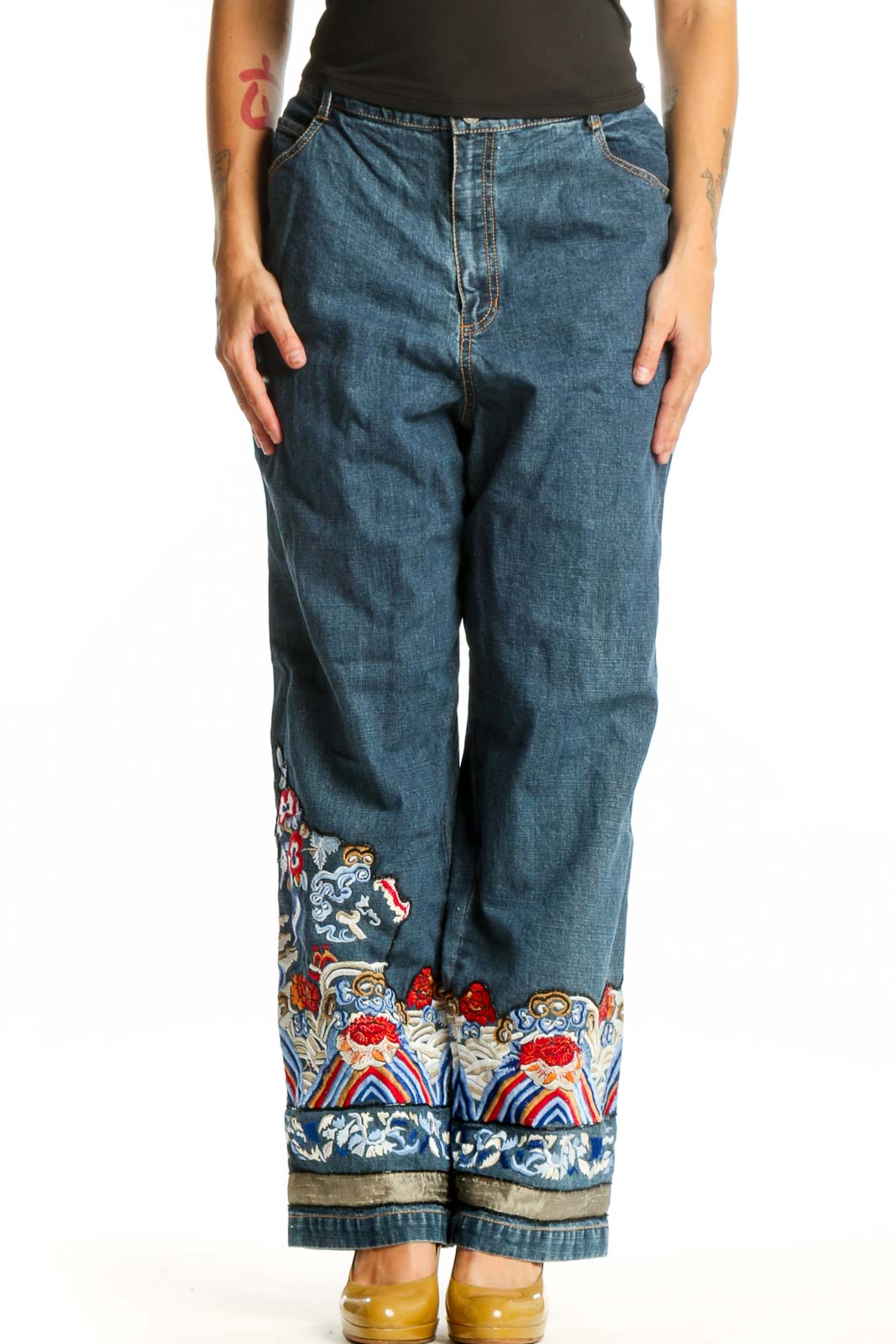 Front view of blue embroidered denim jeans with colorful floral and ornamental design at hem by Chico's Design