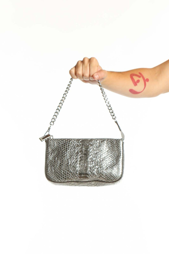 Silver metallic quilted clutch with chain strap held in hand, showing textured finish and elegant design